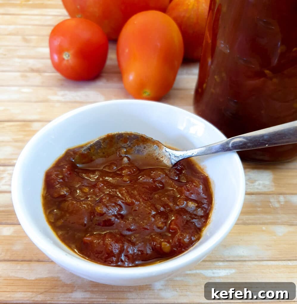 A small white dish filled with tomato jam, with a spoon.
