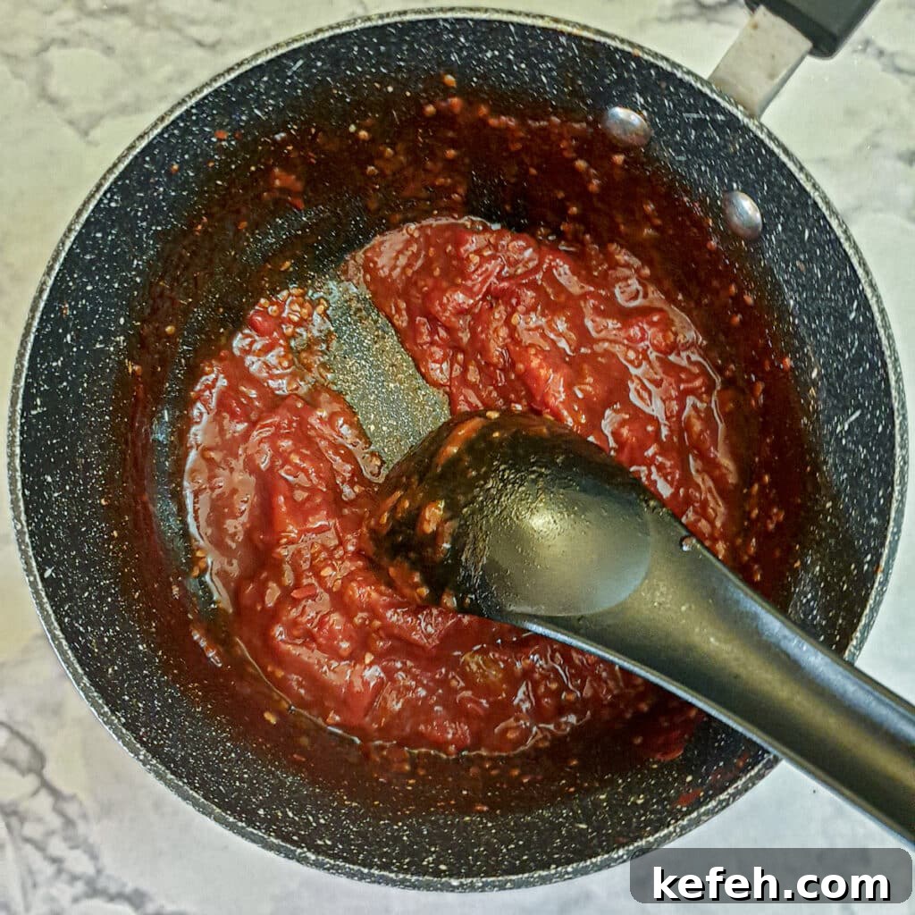 Tomato jam in a saucepan showing how a spatula can be drawn through the jam to leave a trail.