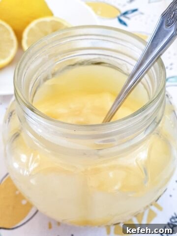 Microwave lemon curd in a glass jar with a spoon.