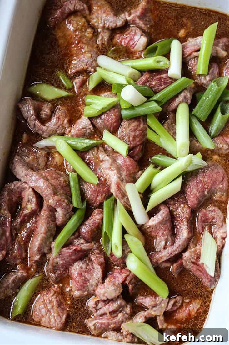 Sliced steak in a crock pot with scallions