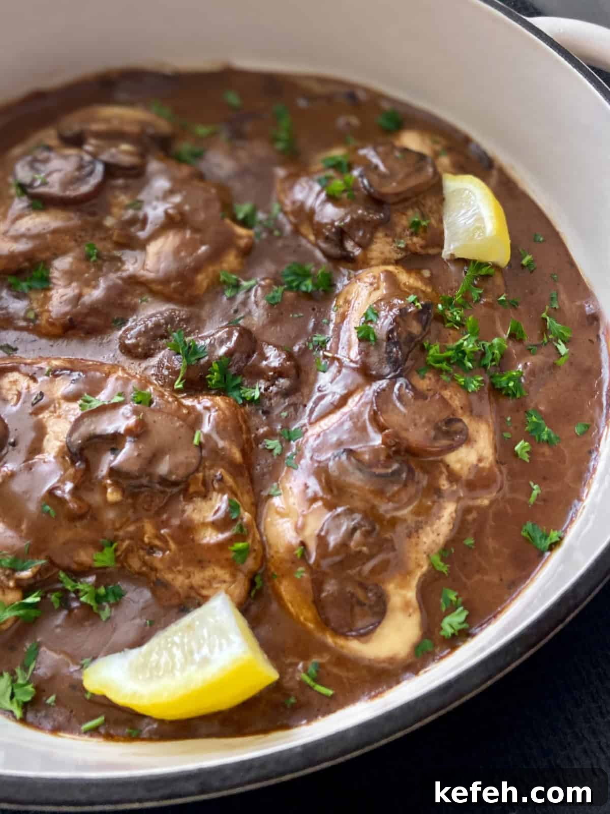 Close up image of balsamic chicken in pan with mushrooms and lemon wedges.
