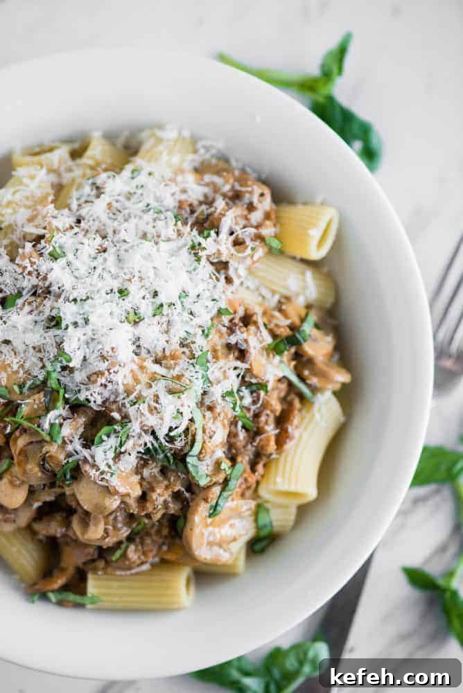 Creamy Sausage Mushroom Rigatoni - easy, delicious dinner in less than 30 minutes Creamy Sausage Mushroom Rigatoni in a white bowl with a metal fork and garnish on the side.