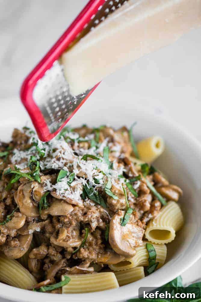 Freshly grated cheese on Creamy Sausage Mushroom Rigatoni Cheese being freshly grated on top of Creamy Sausage Mushroom Rigatoni in a white bowl.