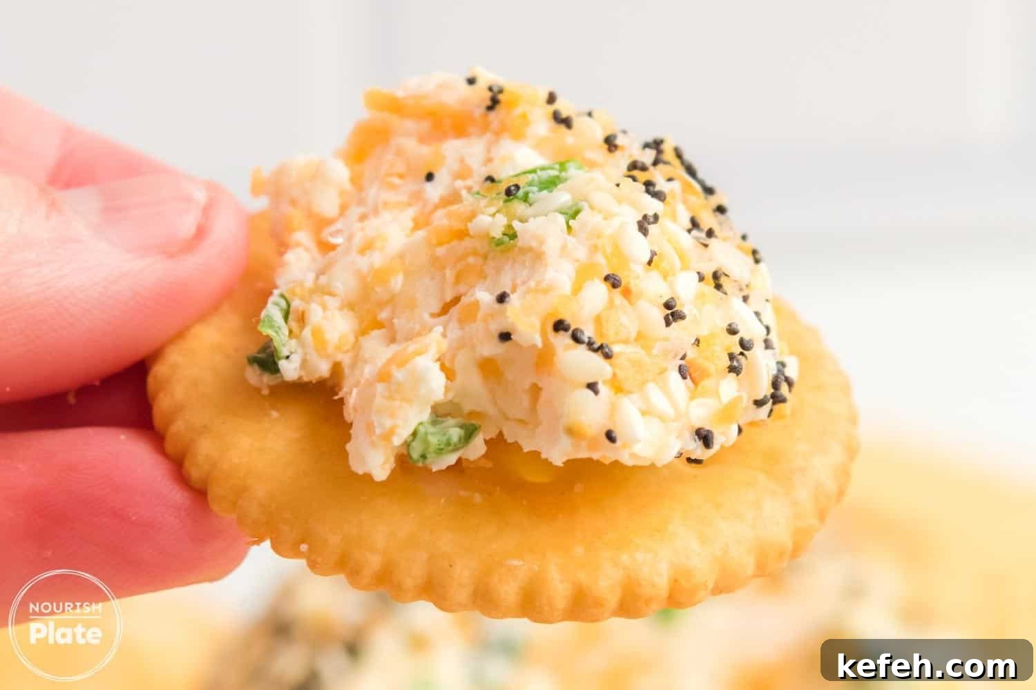 Everything Bagel Cheese Ball Recipe: Creamy Savory Appetizer 4 A close-up of a Ritz cracker topped with a scoop of creamy Everything Bagel Cheese Ball, showing bits of cheddar, scallions, and a coating of sesame seeds, poppy seeds, and garlic flakes.