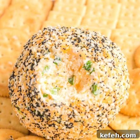 Everything Bagel Cheese Ball Recipe: Creamy Savory Appetizer 5 A round Everything Bagel Cheese Ball coated with sesame seeds, poppy seeds, garlic, and onion seasoning, with a creamy cheese and scallion filling visible in the center, surrounded by buttery Ritz and Club crackers for serving.