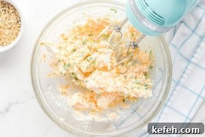 Everything Bagel Cheese Ball Recipe: Creamy Savory Appetizer 6 A mixing bowl filled with a creamy cheese mixture of cream cheese, shredded cheddar, and chopped scallions being blended with an electric hand mixer.