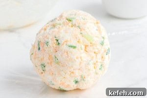 Everything Bagel Cheese Ball Recipe: Creamy Savory Appetizer 7 A smooth cheese ball coated with Everything Bagel seasoning resting on a plate covered with extra seasoning.