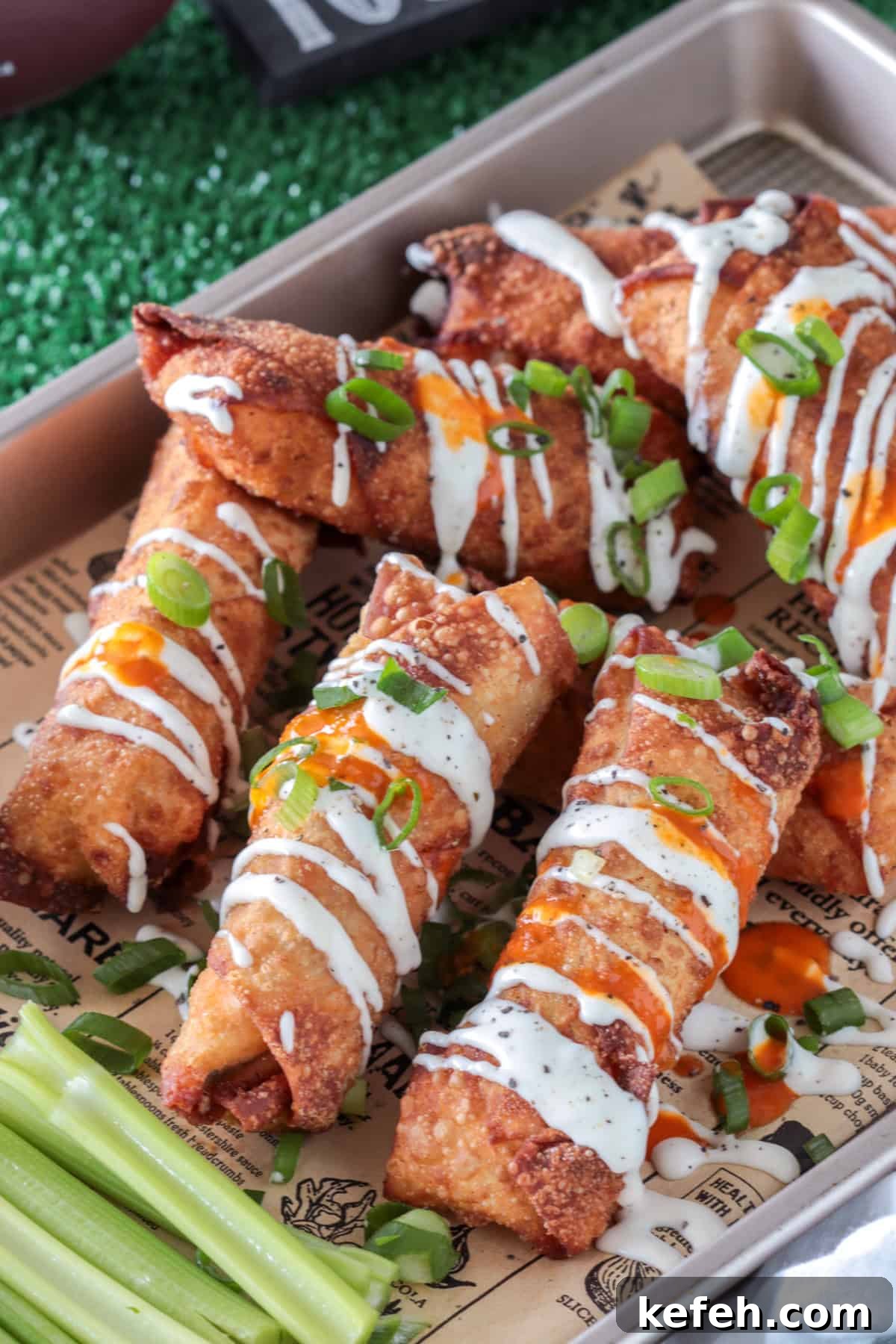 Buffalo chicken egg rolls on paper drizzled with ranch dressing.