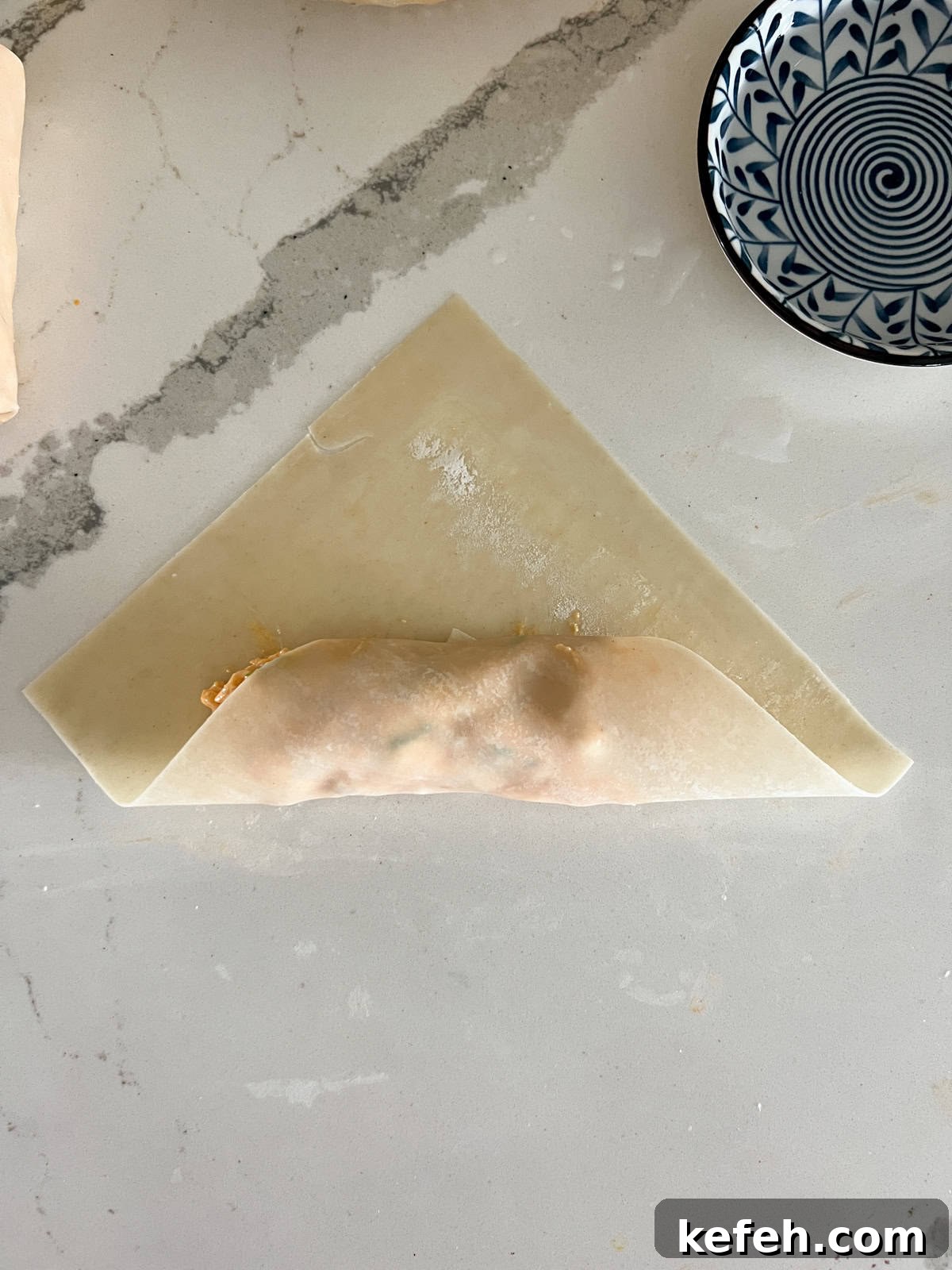 Egg roll wrapper folded up with filling inside.
