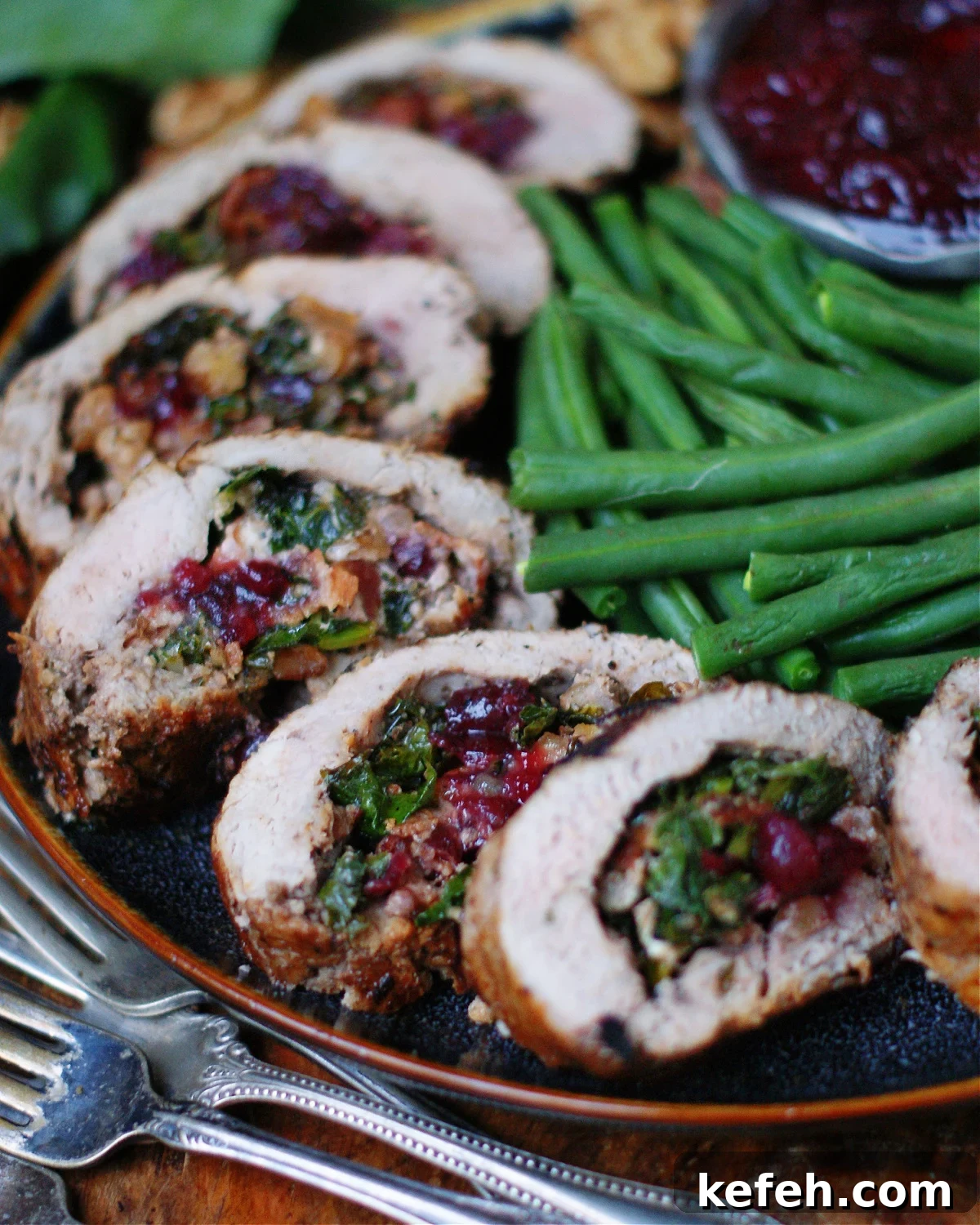 Pork tenderloin stuffed with walnuts, cranberries, goat cheese and collard greens, sliced and shown on platter