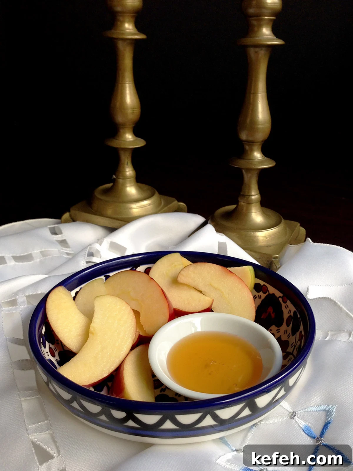 Last-Minute Rosh Hashanah Prep: Quick Guide to Ready Your Home and Table 2 Apples and honey in a blue bowl with two shabbat candlesticks in the background.