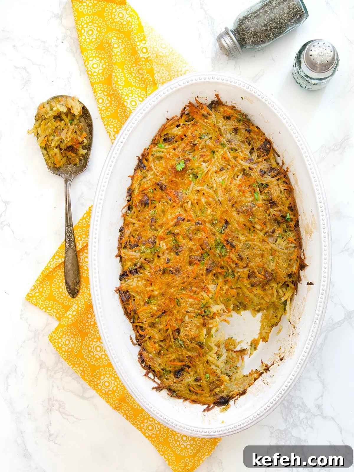 Last-Minute Rosh Hashanah Prep: Quick Guide to Ready Your Home and Table 29 Top down view of a whole oval white pan of potato kugel with a spoon of it on the side and some salt and pepper shakers.
