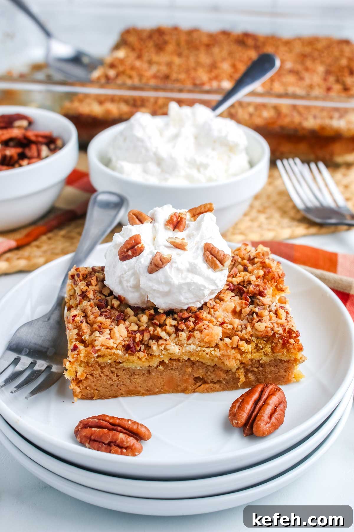 Styled plate with a slice of dump cake topped with whipped cream and pecans, with whipped cream bowl in background.
