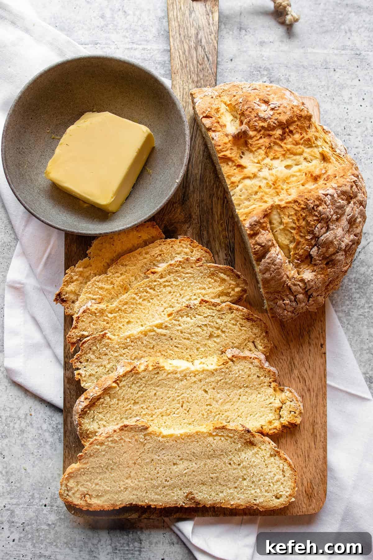 A wooden board with half a loaf of Irish soda bread with slices and a bowl of butter.