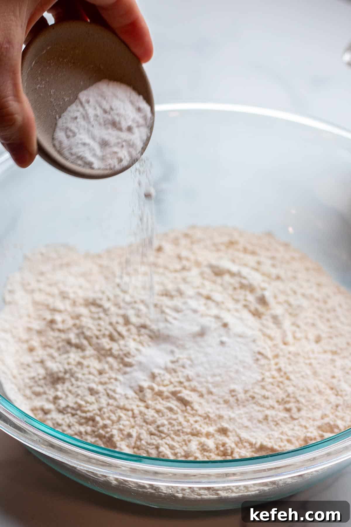Baking soda being added to a bowl of flour.
