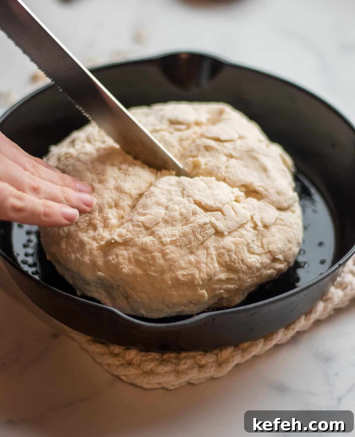 A knife cutting a loaf of soda bread in a cast iron skillet.