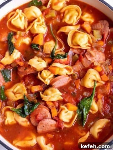 A large white Dutch Oven full of a soup made with tortellini, sausage and spinach.