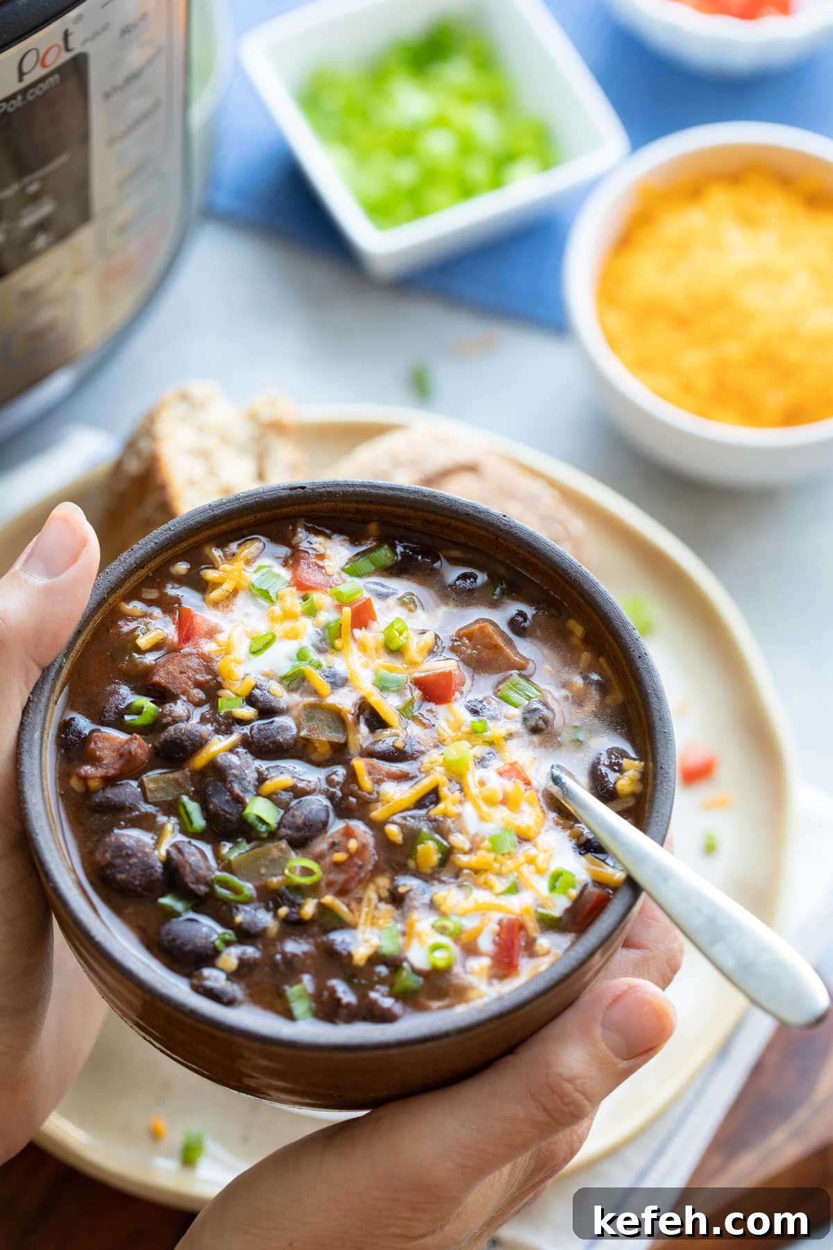 Instant Pot Black Bean Soup Recipe — Quick, Flavorful Meal 10 Two hands lifting bowl of Black Bean Soup that's been garnished with scallions, sour cream and cheese.