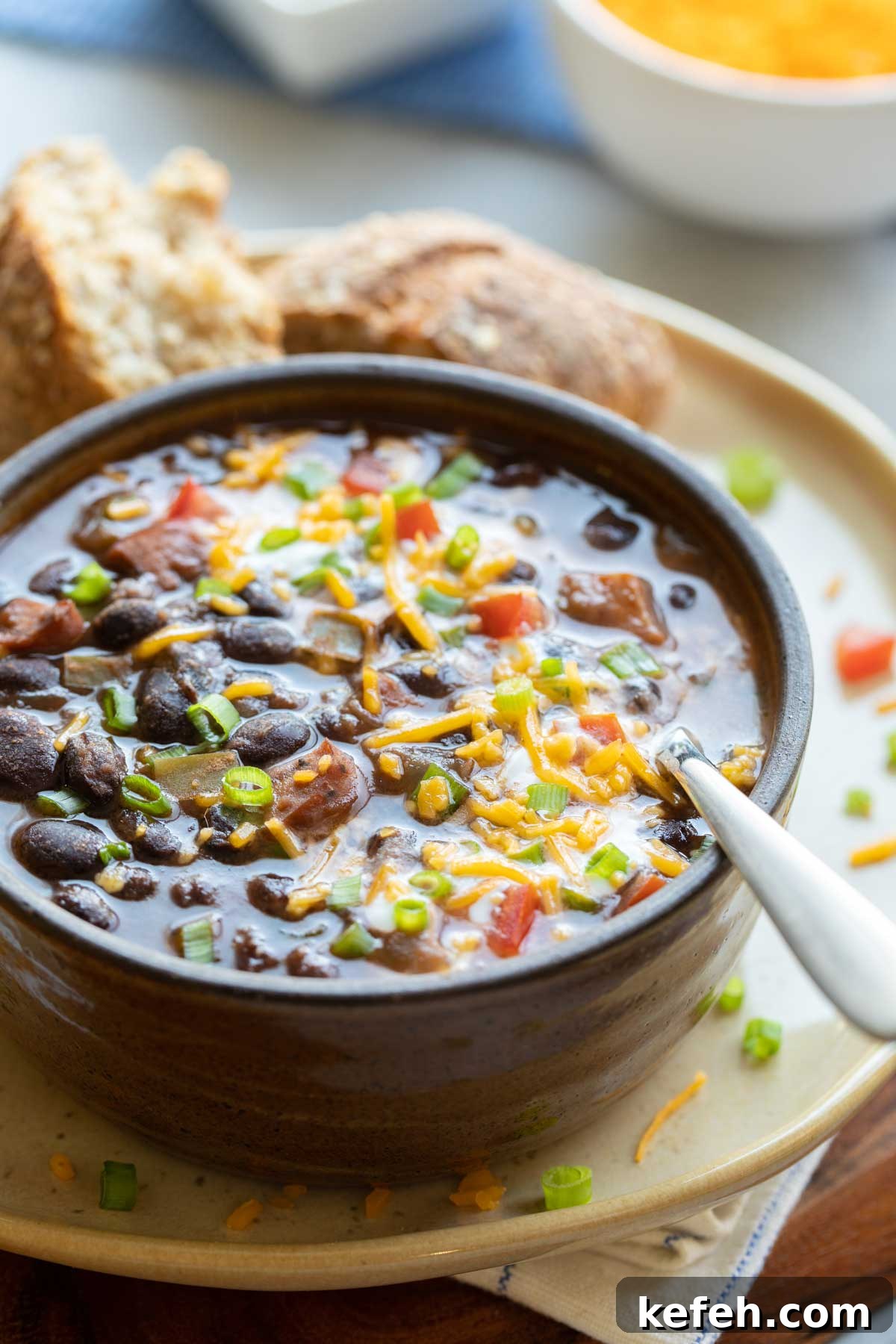 Instant Pot Black Bean Soup Recipe — Quick, Flavorful Meal 8 Black Bean Soup served in brown bowl on yellow plate, with spoon dipped in and roll on the side.