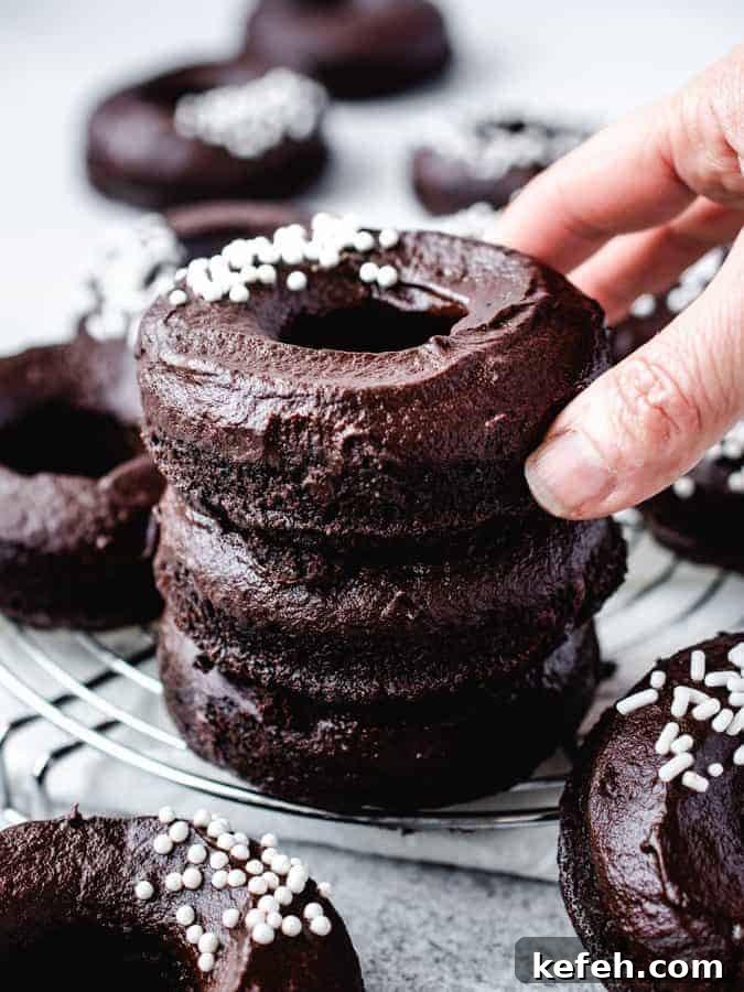 Vegan Baked Chocolate Fudge Doughnuts Recipe 4 stack of 3 chocolate fudge donuts with hand grabbing for top one