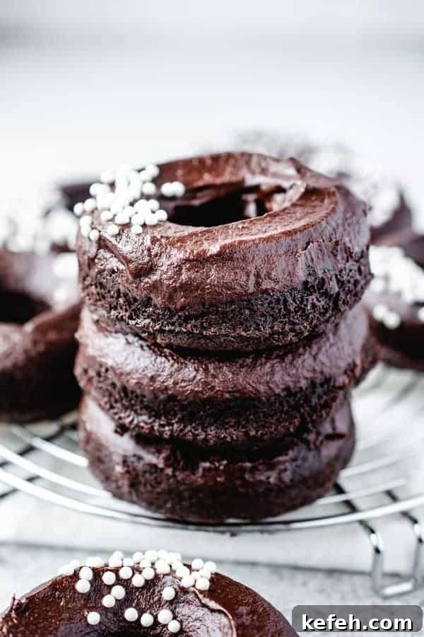 Vegan Baked Chocolate Fudge Doughnuts Recipe 6 stack of three chocolate fudge doughnuts with white sprinkles on a wire rack