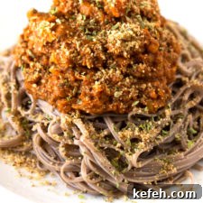 Photo of a dish of vegan bolognese with some pasta and vegan Parmesan cheese.