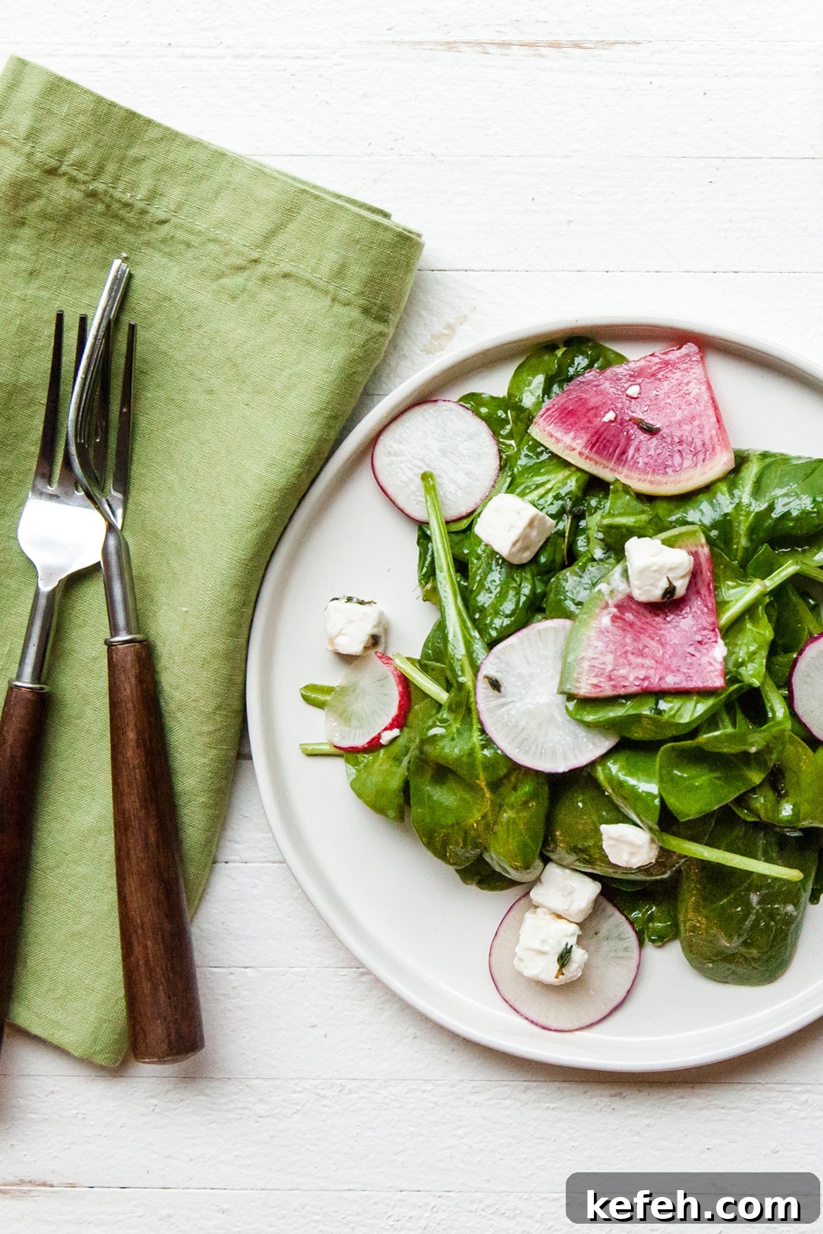 White plate of spinach and radish salad with feta.