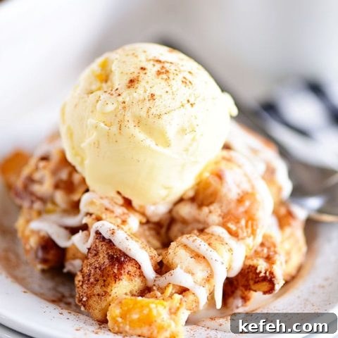 Cinnamon Roll Peach Cobbler topped with ice cream on a white plate