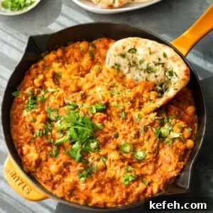 Curry topped with cilantro and serrano slices, served in a skillet with naan.