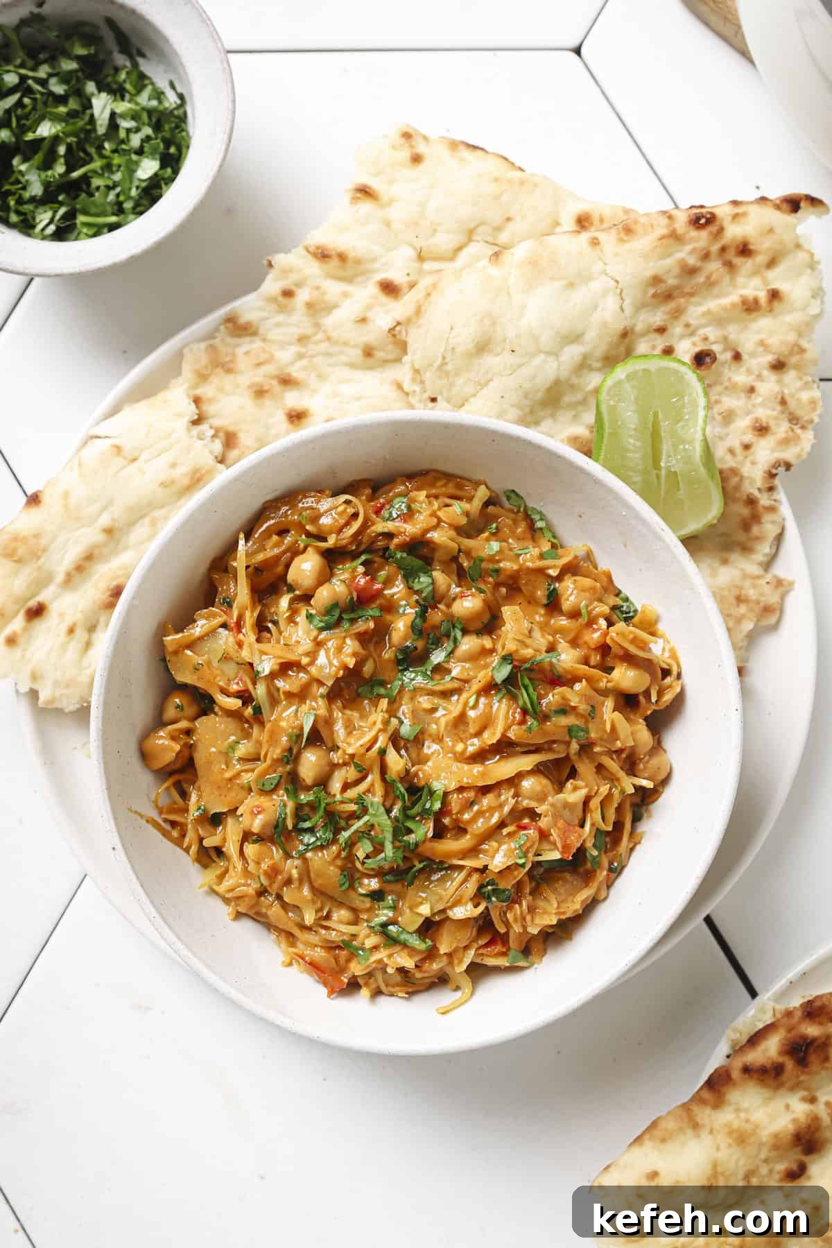 bowl of curry with a side of roti and a lime wedge.