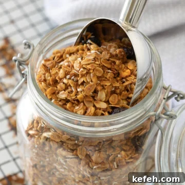 A close up of an open jar of homemade granola with a silver scoop.
