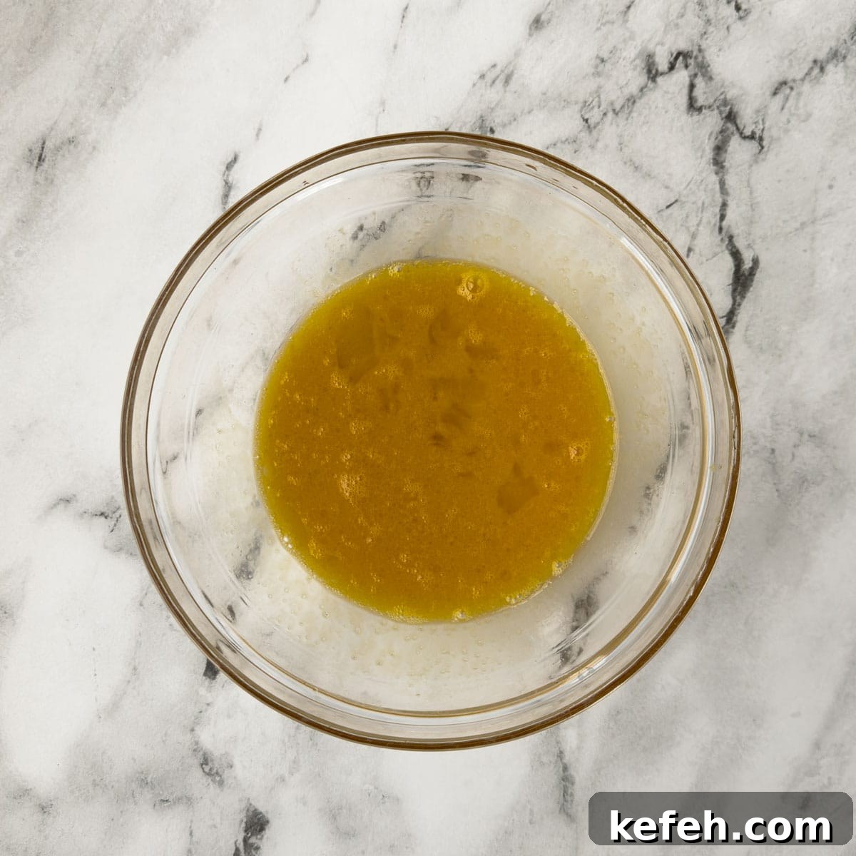 Eggs and oil whisked together in a glass mixing bowl.