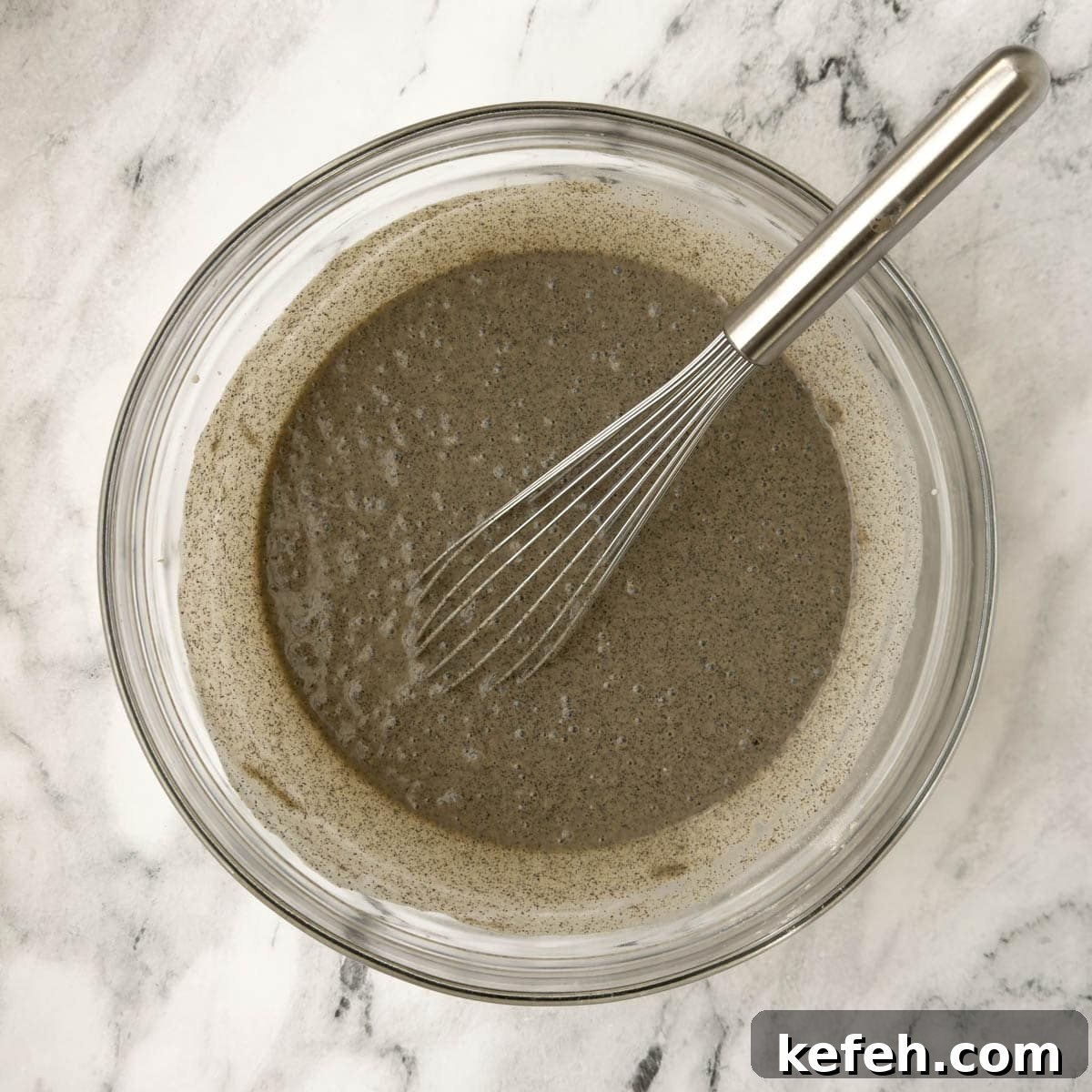 Buckwheat pancake batter mixed in a glass bowl with a silver whisk.