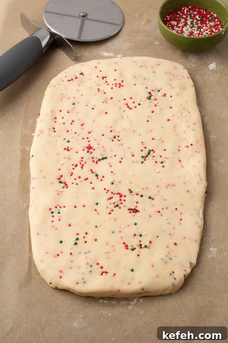 Cookie dough rolled out into a rectangle shape, sitting on parchment paper with a pizza cutter on the side.