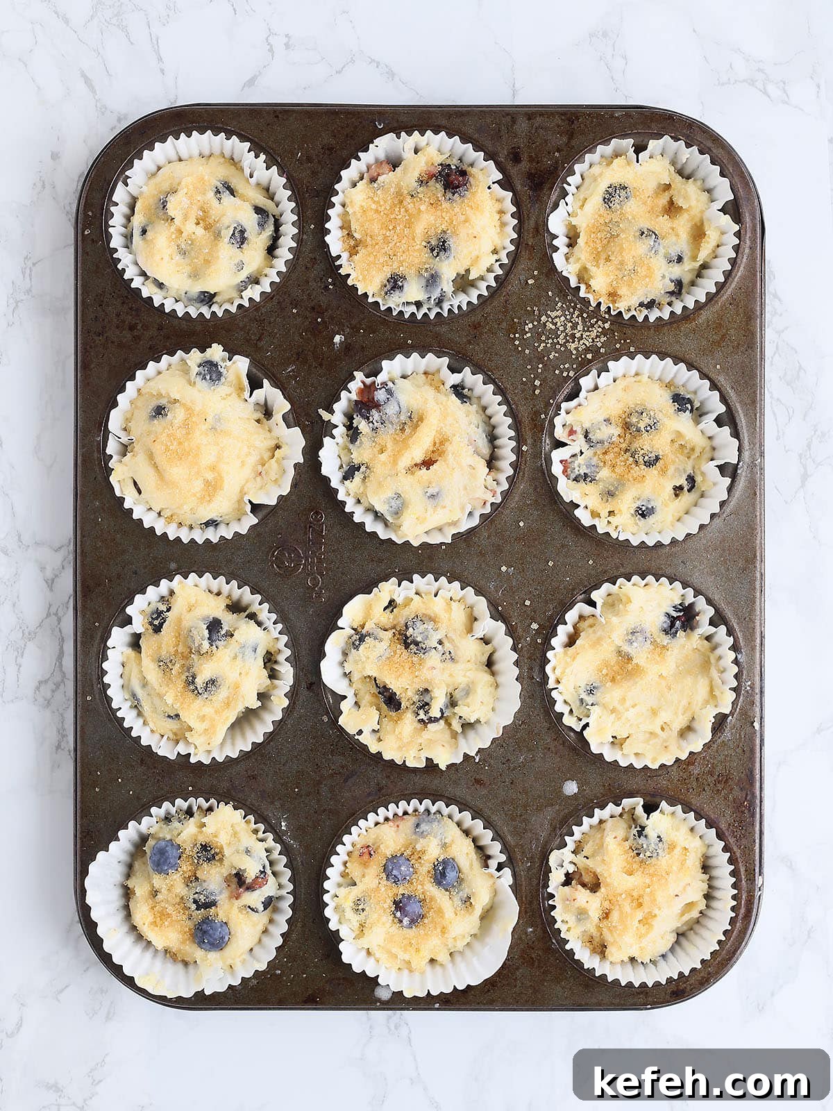 Unbaked muffins topped with sugar in a muffin pan.