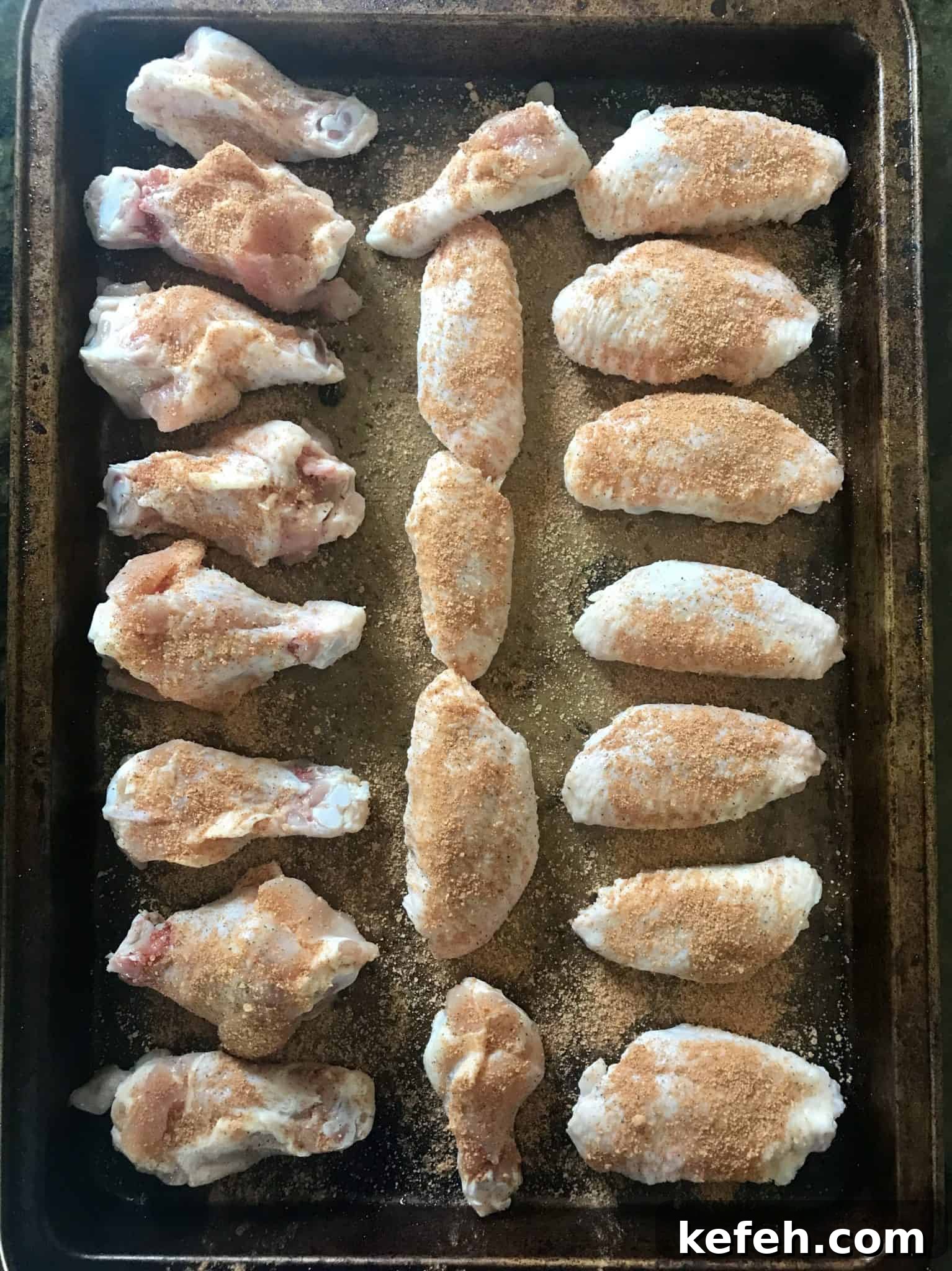 Seasoned chicken wings ready to be cooked lined up on baking sheet overhead shot