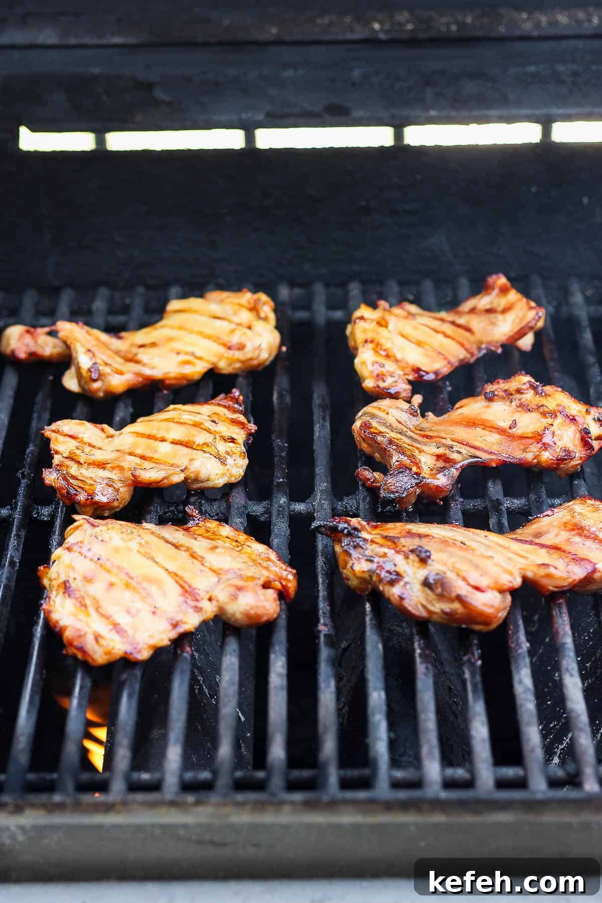 Sticky Grilled Teriyaki Chicken with Charred Scallions 4 Chicken thighs cooking on a gas grill.