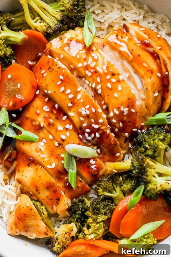 Sticky Grilled Teriyaki Chicken with Charred Scallions 7 Top down shot of a bowl of rice with baked teriyaki chicken and veggies on top with sesame seed garnish.