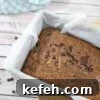 Dairy-free chocolate zucchini bread in a baking loaf with parchment paper and a blue linen and scoop of collagen powder around it.
