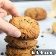 Two fingers placing chocolate chip protein cookie ontop of two others and more on parchment paper behind them.