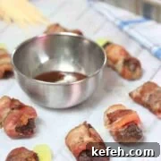Close up of bacon wrapped steak bites on parchment paper with a steel bowl of bbq sauce.