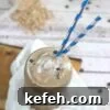 Mason jar with coffee protein shake in it and blue straws on top of white cheesecloth on a cutting board with protein powder and chocolate chips around it.