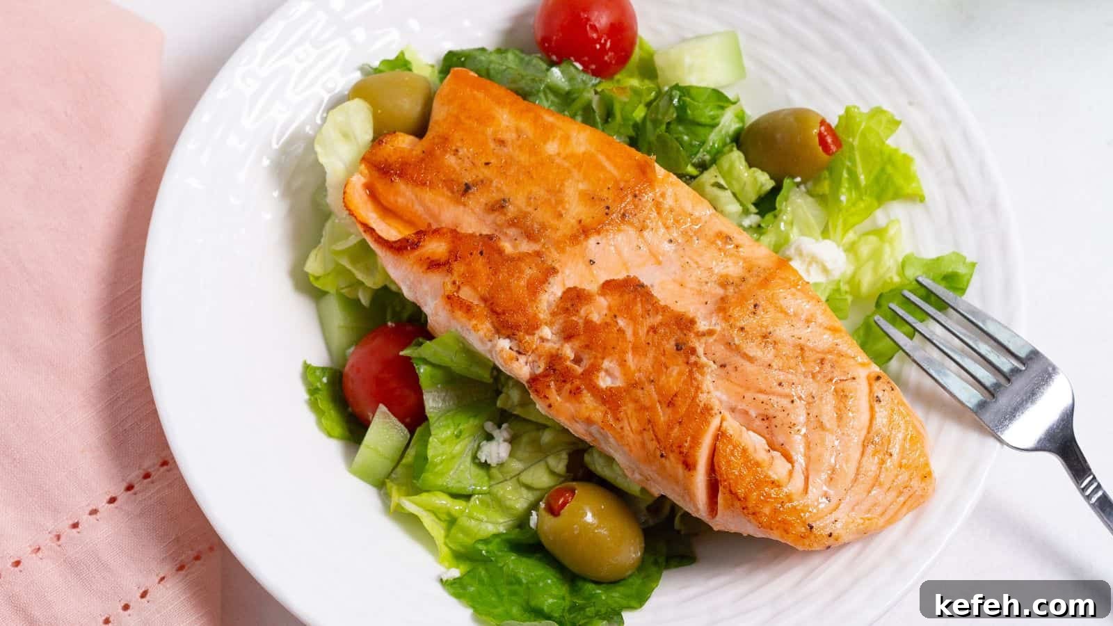 30 Seafood Recipes That Turn Weeknights Into a Vacation 28 A grilled salmon fillet served on a bed of fresh salad with lettuce, tomatoes, and olives on a white plate.