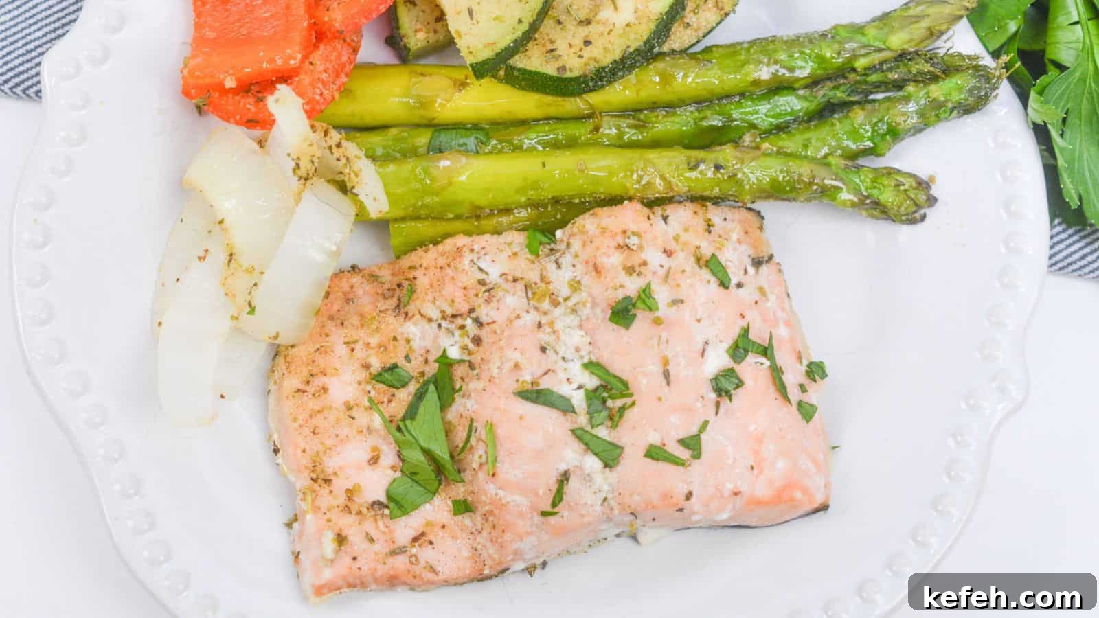 30 Seafood Recipes That Turn Weeknights Into a Vacation 4 Baked salmon fillet with asparagus, zucchini, and bell peppers on a white plate, garnished with herbs.
