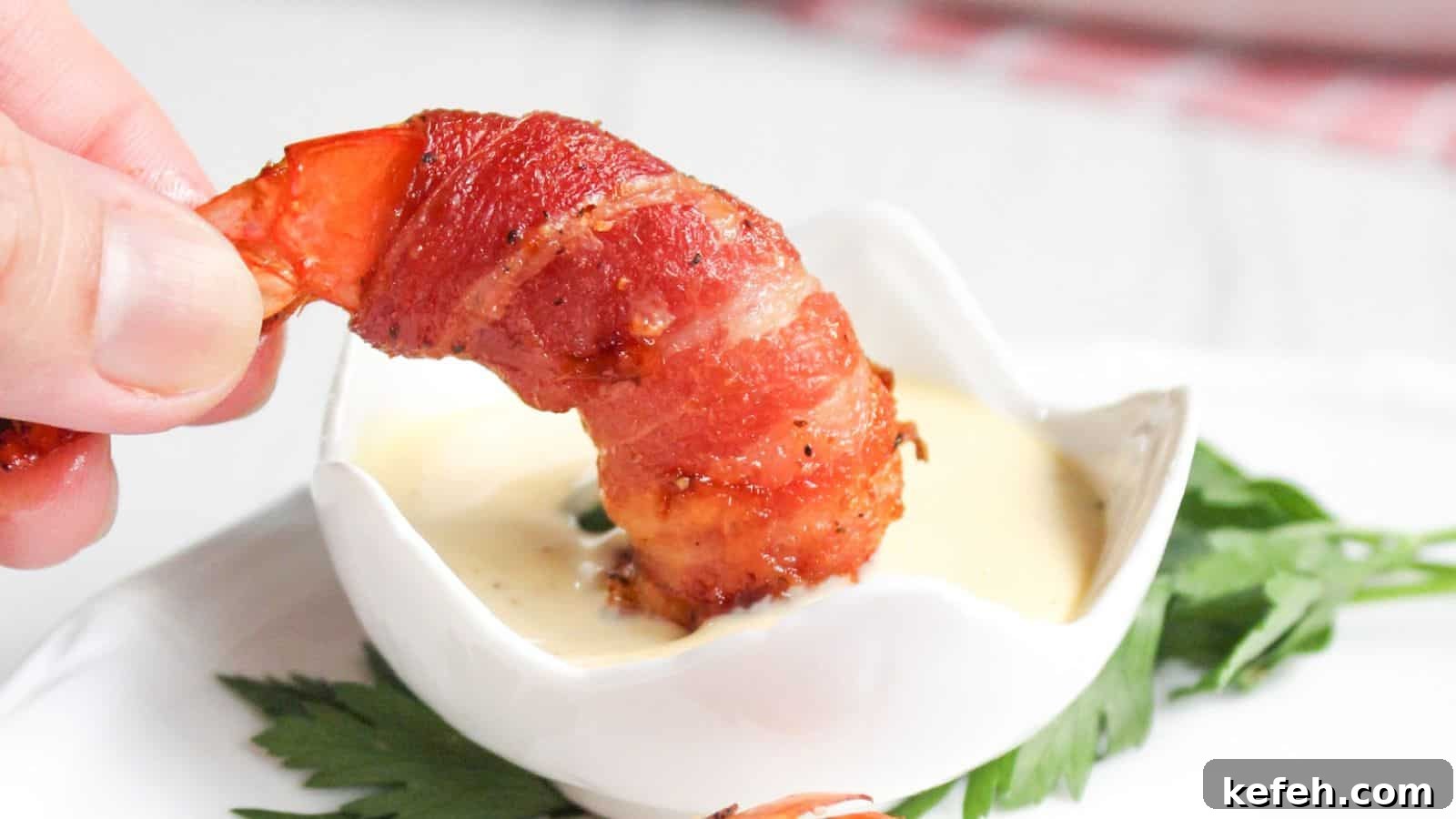 30 Seafood Recipes That Turn Weeknights Into a Vacation 6 A hand holding a bacon-wrapped shrimp dipped in a small bowl of sauce, with a green leaf garnish on the side.