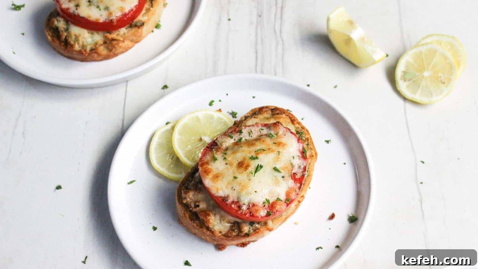 30 Seafood Recipes That Turn Weeknights Into a Vacation 7 Two plates of crab melt with sliced tomatoes and melted cheese, garnished with lemon slices on a white wooden surface.