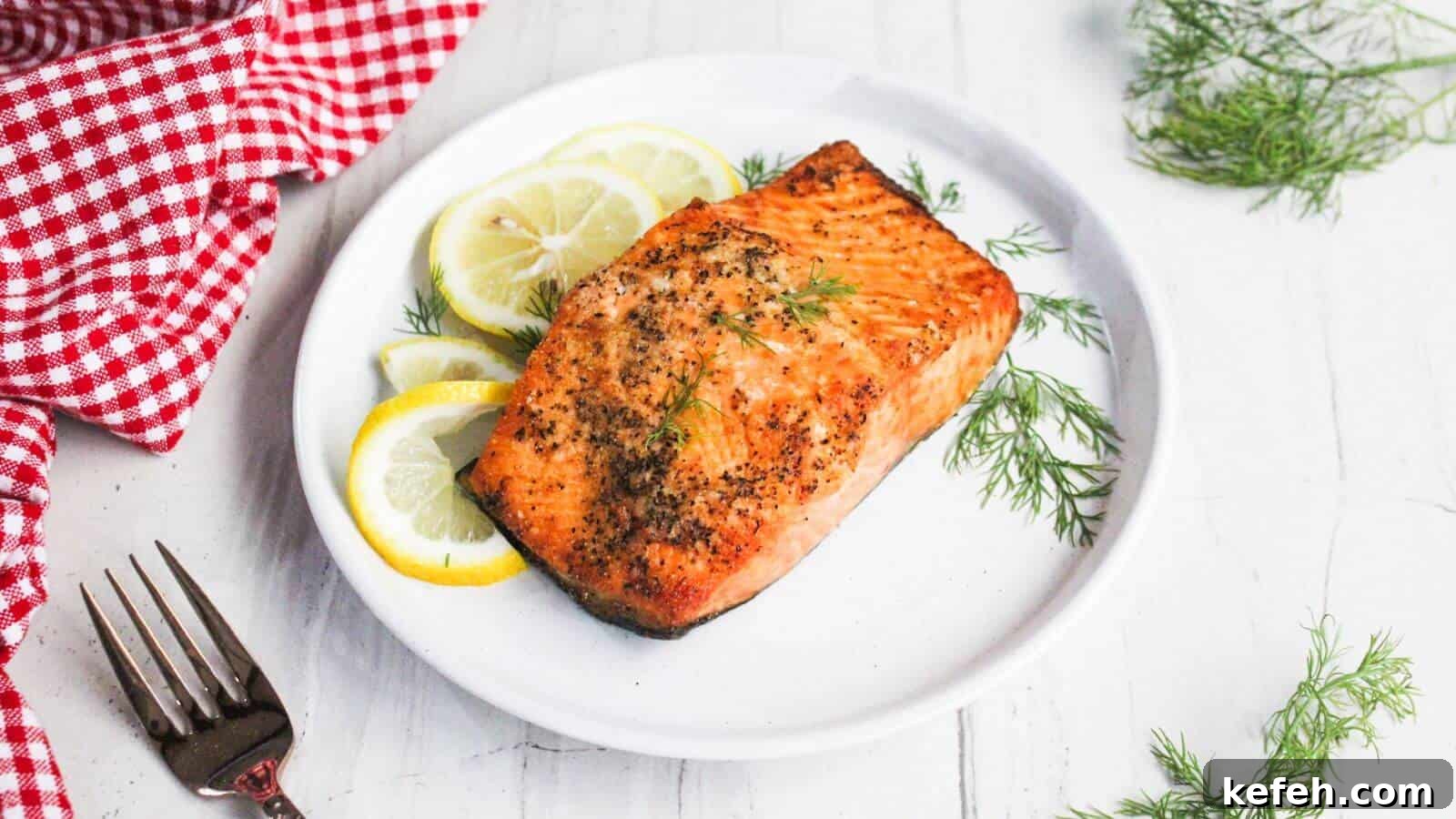 30 Seafood Recipes That Turn Weeknights Into a Vacation 8 Grilled salmon fillet on a white plate garnished with lemon slices and dill, next to a red checkered cloth and a fork.