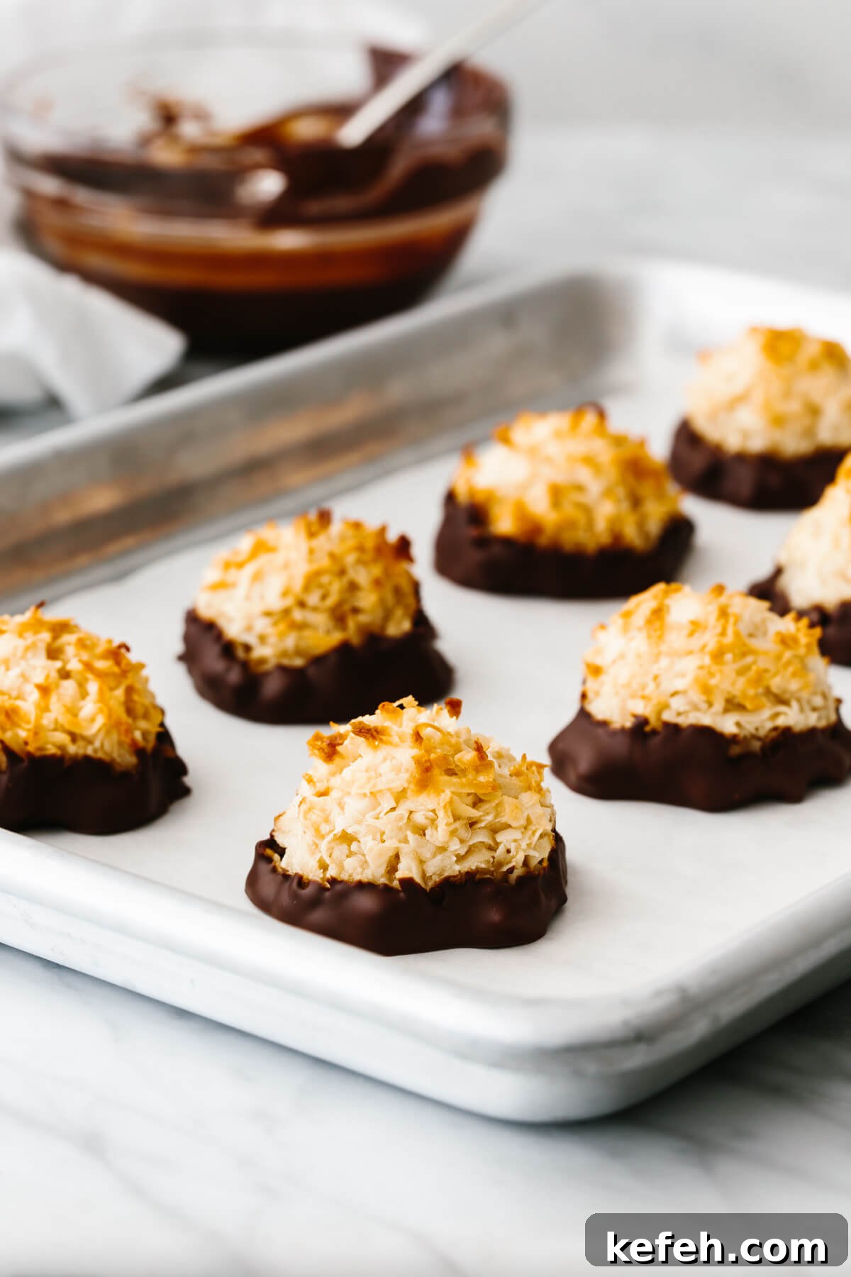 25+ Unique Thanksgiving Dessert Ideas to Impress Your Guests 5 Coconut macaroons on a baking sheet next to a bowl of chocolate.