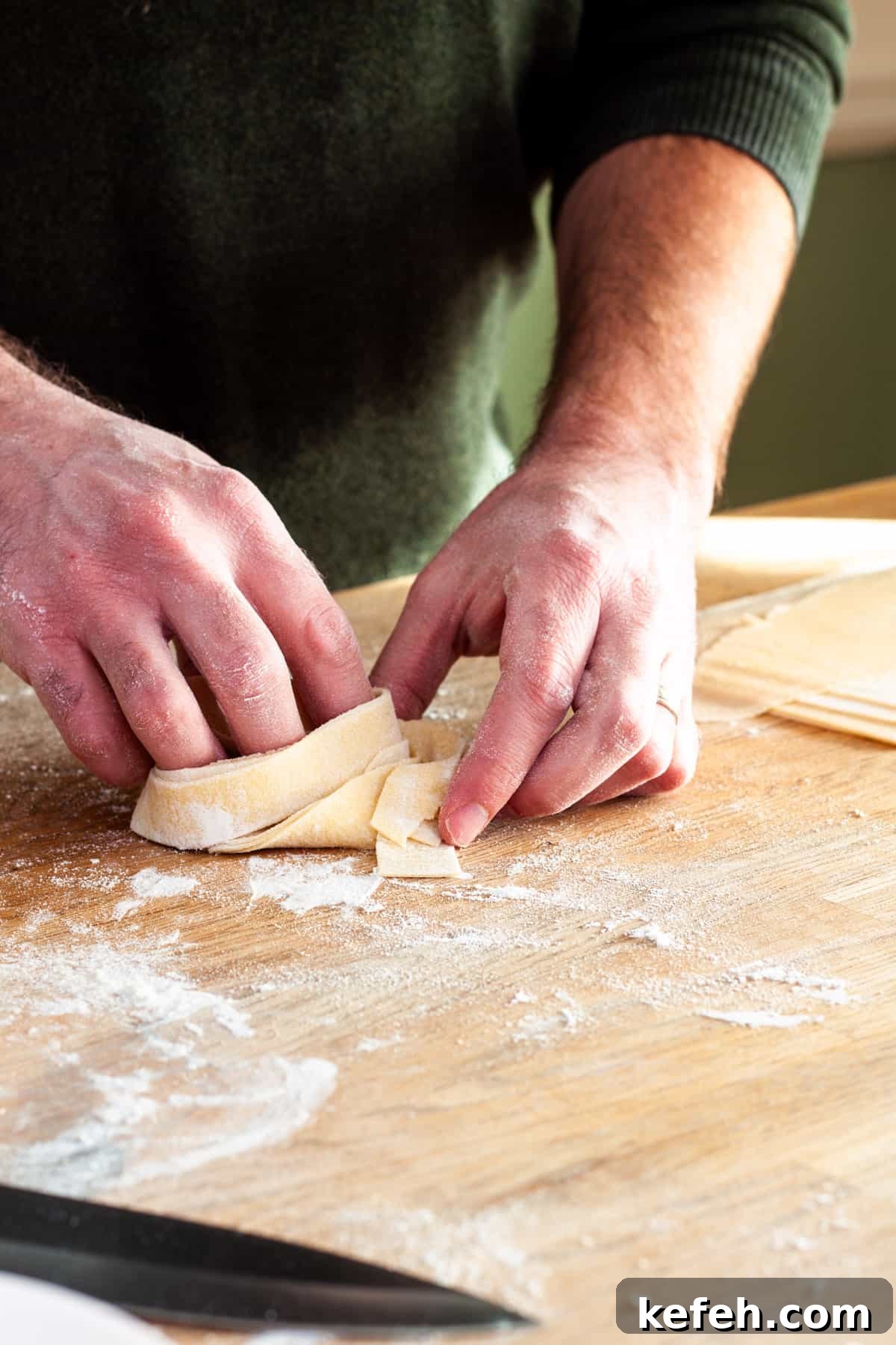 A nest of homemade fresh pappardelle getting turned together on a cutting board.