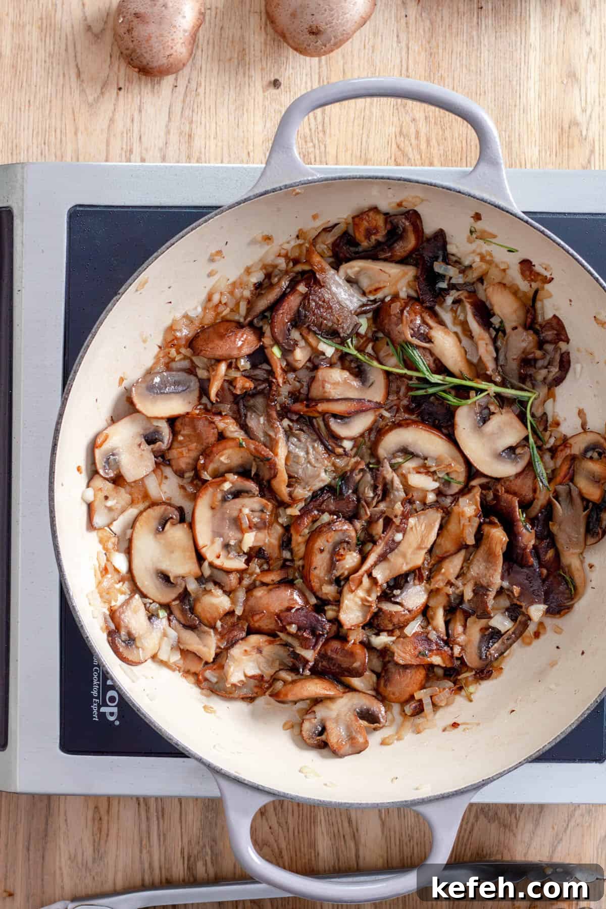 Seared mushrooms in a large skillet with herbs and garlic.